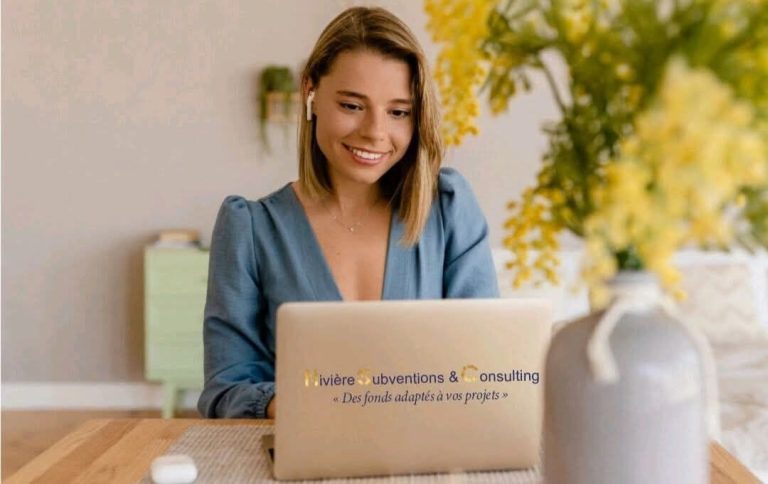 Subventions Femme souriante travaillant sur un ordinateur portable avec un vase de fleurs à proximité.